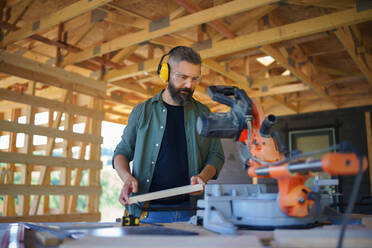 Bauarbeiter bei der Arbeit mit der elektrischen Säge in der Holzkonstruktion des Hauses, diy umweltfreundliche Häuser Konzept. - HPIF01525