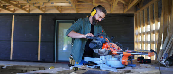 Bauarbeiter arbeitet mit elektrischer Säge in einer Holzkonstruktion eines Hauses, diy umweltfreundliche Häuser Konzept. - HPIF01527