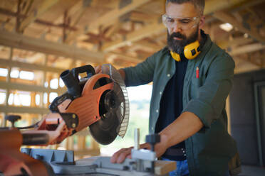Bauarbeiter bei der Arbeit mit der elektrischen Säge in der Holzkonstruktion des Hauses, diy umweltfreundliche Häuser Konzept. - HPIF01529