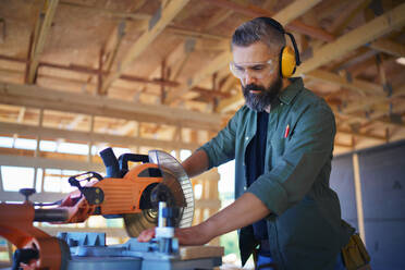 Construction worker working with the eletric saw inside wooden construction of house, diy eco-friendly homes concept. - HPIF01530