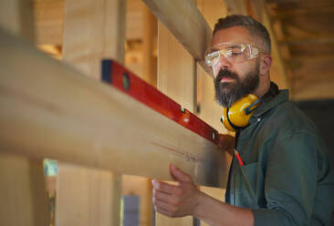 Carpenter checking a wooden planks with spirit level, diy eco-friendly homes concept. - HPIF01538