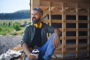 Ein Handwerker, der sich ausruht und eine Pause macht, während er auf einer Holzbaustelle arbeitet, diy eco-friendly homes concept. - HPIF01545