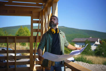 Handyman chcecking blueprints and working on a wooden construction site, diy eco-friendly homes concept. - HPIF01547