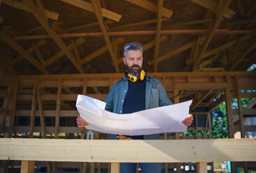 Handyman chcecking blueprints and working on a wooden construction site, diy eco-friendly homes concept. - HPIF01548