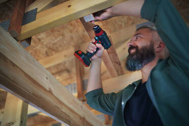 Ein Bauarbeiter arbeitet mit Schraubenzieher auf Holzrahmen, diy umweltfreundliche Häuser Konzept. - HPIF01556