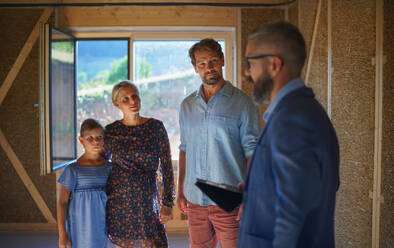 Ein Handelsvertreter zeigt einer jungen Familie auf der Baustelle die Pläne eines neuen Hauses. - HPIF01562