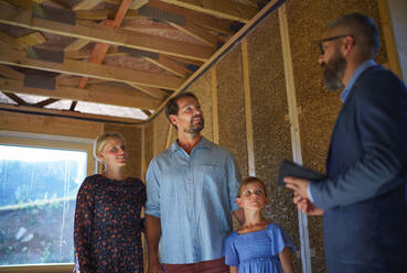 Ein Handelsvertreter zeigt einer jungen Familie auf der Baustelle die Pläne eines neuen Hauses. - HPIF01565
