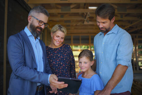 A sales Agent showing plans of new house to young family on construction site. - HPIF01566