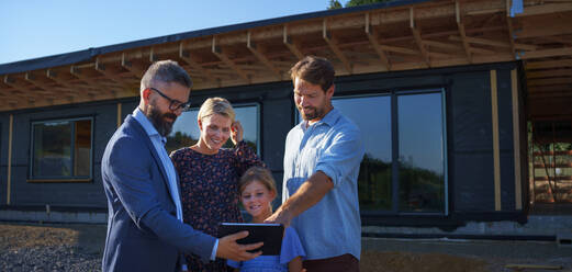 A sales Agent showing plans of new house to young family on construction site. - HPIF01573