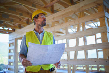 Bauingenieur oder Architekt mit Bauplänen, der die Öko-Baustelle eines Holzhauses besucht und prüft. - HPIF01590