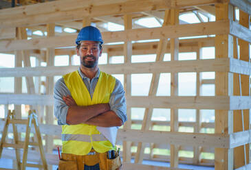 Construction worker in protective clothes posing in unfinished eco wooden house. - HPIF01591