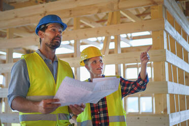 Bauingenieure oder Architekten mit Bauplänen, die eine Baustelle für ein Holzrahmenhaus prüfen - HPIF01592