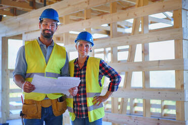 Bauingenieure oder Architekten mit Bauplänen bei der Besichtigung einer Baustelle für ein Holzrahmenhaus - HPIF01593