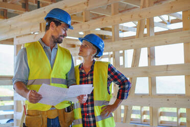 Bauingenieure oder Architekten mit Bauplänen, die eine Baustelle für ein Holzrahmenhaus prüfen - HPIF01594
