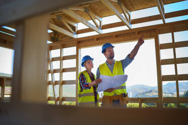 Bauingenieure oder Architekten mit Bauplänen, die eine Baustelle für ein Holzrahmenhaus besichtigen und besichtigen - HPIF01595