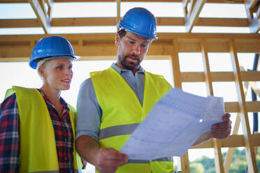 Bauingenieure oder Architekten mit Bauplänen, die eine Baustelle für ein Holzrahmenhaus prüfen - HPIF01596