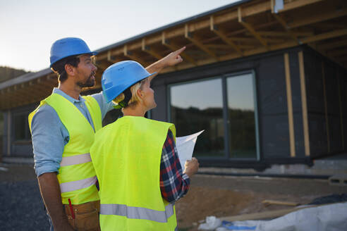 Bauingenieure oder Architekten mit Bauplänen, die eine Baustelle für ein Holzrahmenhaus prüfen - HPIF01599