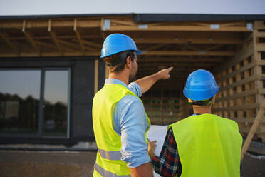 Bauingenieure oder Architekten mit Bauplänen, die eine Baustelle für ein Holzrahmenhaus prüfen - HPIF01600