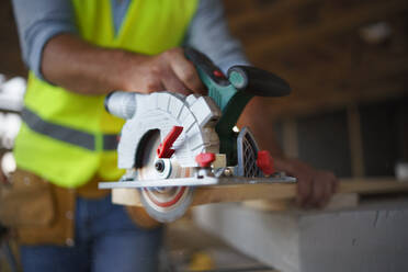 Close-up of construction worker working with the eletric saw inside wooden construction of house, diy eco-friendly homes concept. - HPIF01605