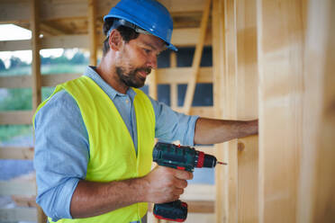 A construction worker working with screwdriver on wooden frame, diy eco-friendly homes concept. - HPIF01609