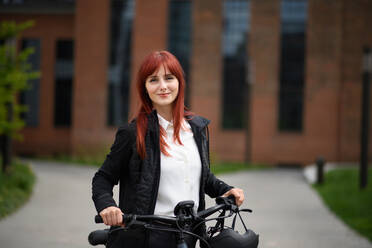 Porträt einer Geschäftsfrau, die mit dem Fahrrad zur Arbeit fährt und dabei in die Kamera schaut, Konzept des nachhaltigen Lebensstils. - HPIF01616