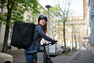 Eine Kurierin auf dem Fahrrad mit Thermorucksack auf dem Weg zur Auslieferung von Lebensmitteln an Kunden. - HPIF01619