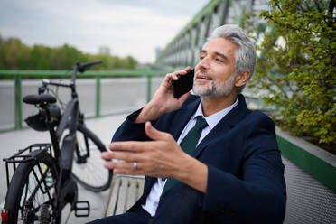 A businessman with bike sitting on bench, using smartphone. Commuting and alternative transport concept - HPIF01622