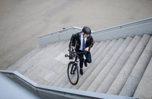 Ein Geschäftsmann auf dem Weg zur Arbeit, der sein Fahrrad nach oben trägt, ein nachhaltiges Lebensstilkonzept. - HPIF01624