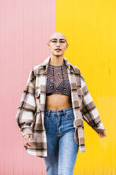 Woman with shaved head walking in front of wall - DAMF01170