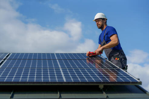 A man worker installing solar photovoltaic panels on roof, alternative energy concept. - HPIF01637