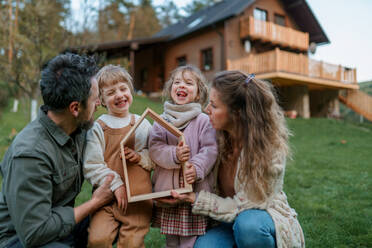 Eine glückliche Familie steht neben ihrem modernen Haus, lächelt und schaut in die Kamera - HPIF01668