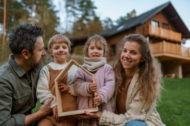Eine glückliche Familie steht neben ihrem modernen Haus, lächelt und schaut in die Kamera - HPIF01669