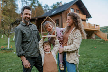 A happy family is standing near their modern house, smiling and looking at camera - HPIF01671