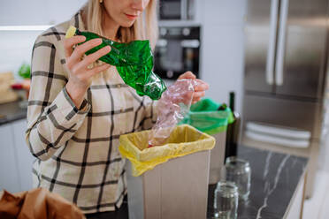Mittelteil einer Frau, die eine leere Plastikflasche in die Recycling-Tonne in der Küche wirft. - HPIF01683