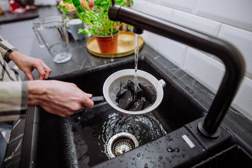 Eine Frau reinigt Shungit-Steine in einem Sieb und gießt Wasser in ein Waschbecken. - HPIF01698