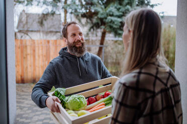 A mature man holding crate with vegetales and fruit and delivering it to woman standing at doorway. - HPIF01717