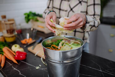 Eine Frau wirft Gemüseschnipsel in einen Kompostkübel in der Küche. - HPIF01720
