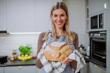 Eine glückliche Frau mit selbstgebackenem Sauerteigbrot in der Hand, die zu Hause kocht. - HPIF01727