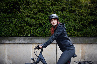 Porträt einer Geschäftsfrau, die mit dem Fahrrad zur Arbeit fährt und dabei in die Kamera schaut, Konzept des nachhaltigen Lebensstils. - HPIF01730
