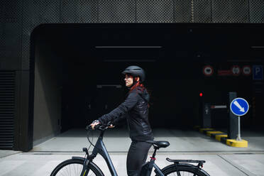 Porträt einer Geschäftsfrau, die mit dem Fahrrad zur Arbeit fährt und dabei in die Kamera schaut, Konzept des nachhaltigen Lebensstils. - HPIF01731