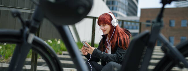 Porträt einer Geschäftsfrau, die mit dem Fahrrad zur Arbeit fährt und sich ausruht, um Musik zu hören, Konzept des nachhaltigen Lebensstils, Weitwinkelaufnahme. - HPIF01732