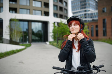 Porträt einer Geschäftsfrau, die auf dem Weg zur Arbeit einen Fahrradhelm aufsetzt, Konzept des nachhaltigen Lebensstils. - HPIF01734