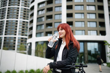 A portrait of businesswoman commuter on the way to work with bike, drinking water, sustainable lifestyle concept. - HPIF01737