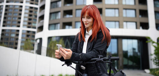 Porträt einer Geschäftsfrau, die mit dem Fahrrad zur Arbeit fährt und dabei ihr Smartphone benutzt, Konzept des nachhaltigen Lebensstils. - HPIF01738