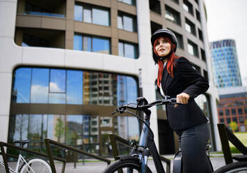 Porträt einer Geschäftsfrau, die mit dem Fahrrad zur Arbeit fährt und dabei in die Kamera schaut, Konzept des nachhaltigen Lebensstils. - HPIF01743