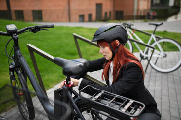 Porträt einer Geschäftsfrau auf dem Weg zur Arbeit, die ihr Fahrrad auf den Ständer stellt, Konzept des nachhaltigen Lebensstils. - HPIF01745