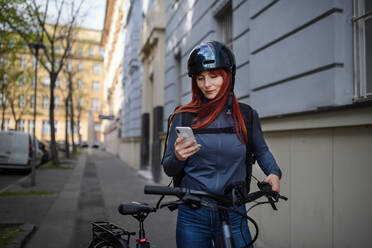 Porträt einer Geschäftsfrau, die mit dem Fahrrad zur Arbeit fährt und dabei ihr Smartphone benutzt, Konzept des nachhaltigen Lebensstils. - HPIF01759