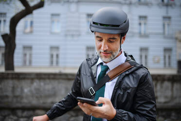 Porträt eines Geschäftsmannes auf dem Weg zur Arbeit, der sein Fahrrad schiebt und mit seinem Handy telefoniert, ein Konzept für nachhaltigen Lebensstil. - HPIF01765