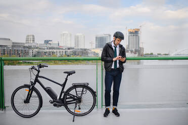 A businessman commuter on the way to work, standing on bridge and texting on mobile phone, sustainable lifestyle concept. - HPIF01769