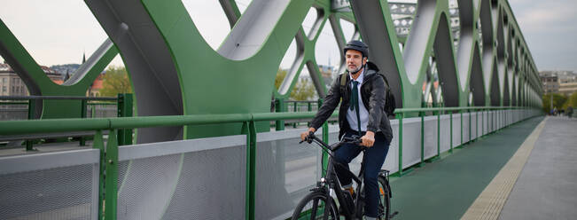 Ein Geschäftsmann auf dem Weg zur Arbeit, mit dem Fahrrad über eine Brücke, nachhaltiger Lebensstil Konzept. - HPIF01772